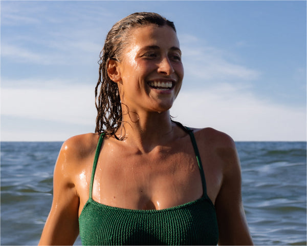 Smiling woman standing in the ocean after a swim, introducing the wellness benefits of ocean swimming.